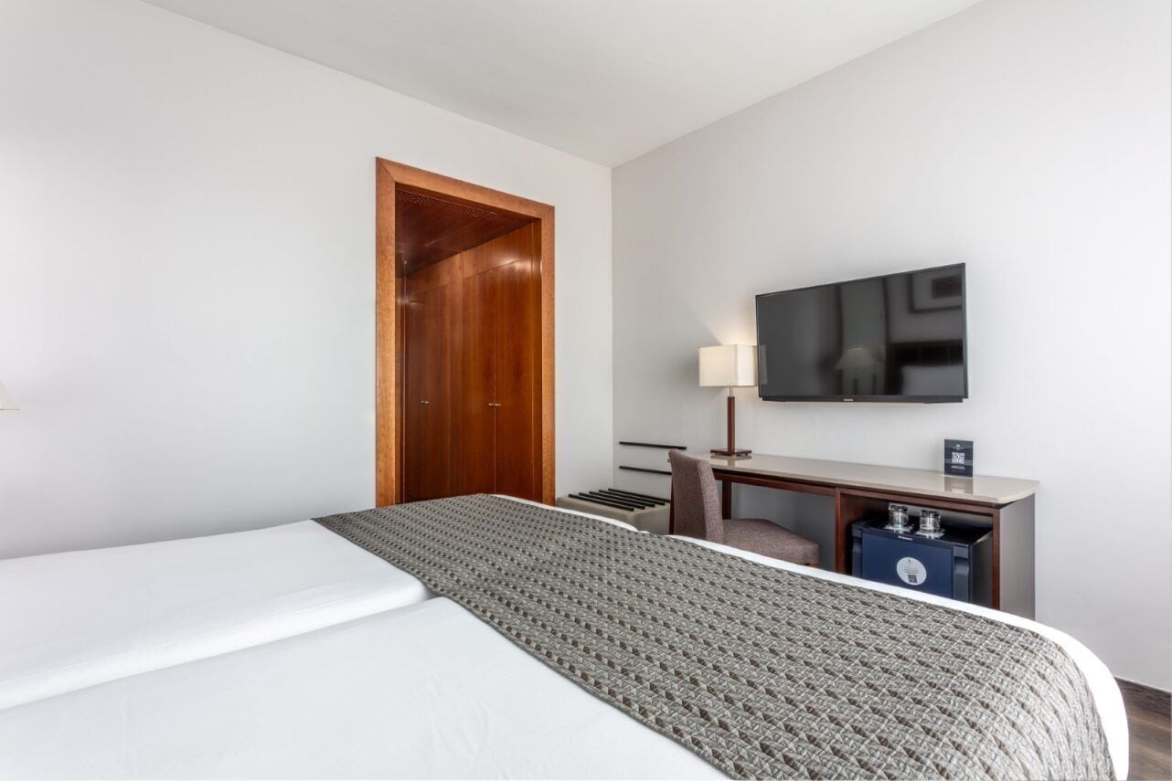 A hotel room with a bed, a desk with a TV, and a wardrobe.