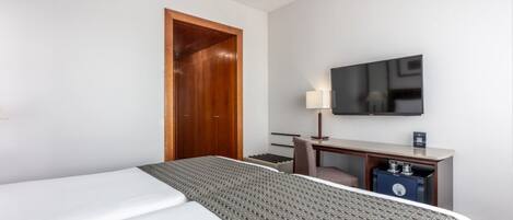 A hotel room with a bed, a desk with a TV, and a wardrobe.