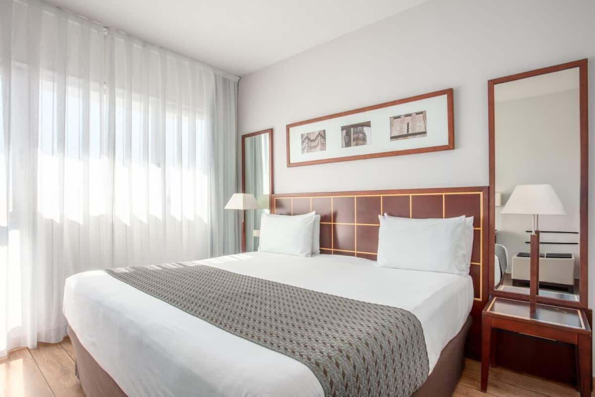 A hotel room with a large bed, a wooden headboard, two bedside tables with lamps, and a large mirror.