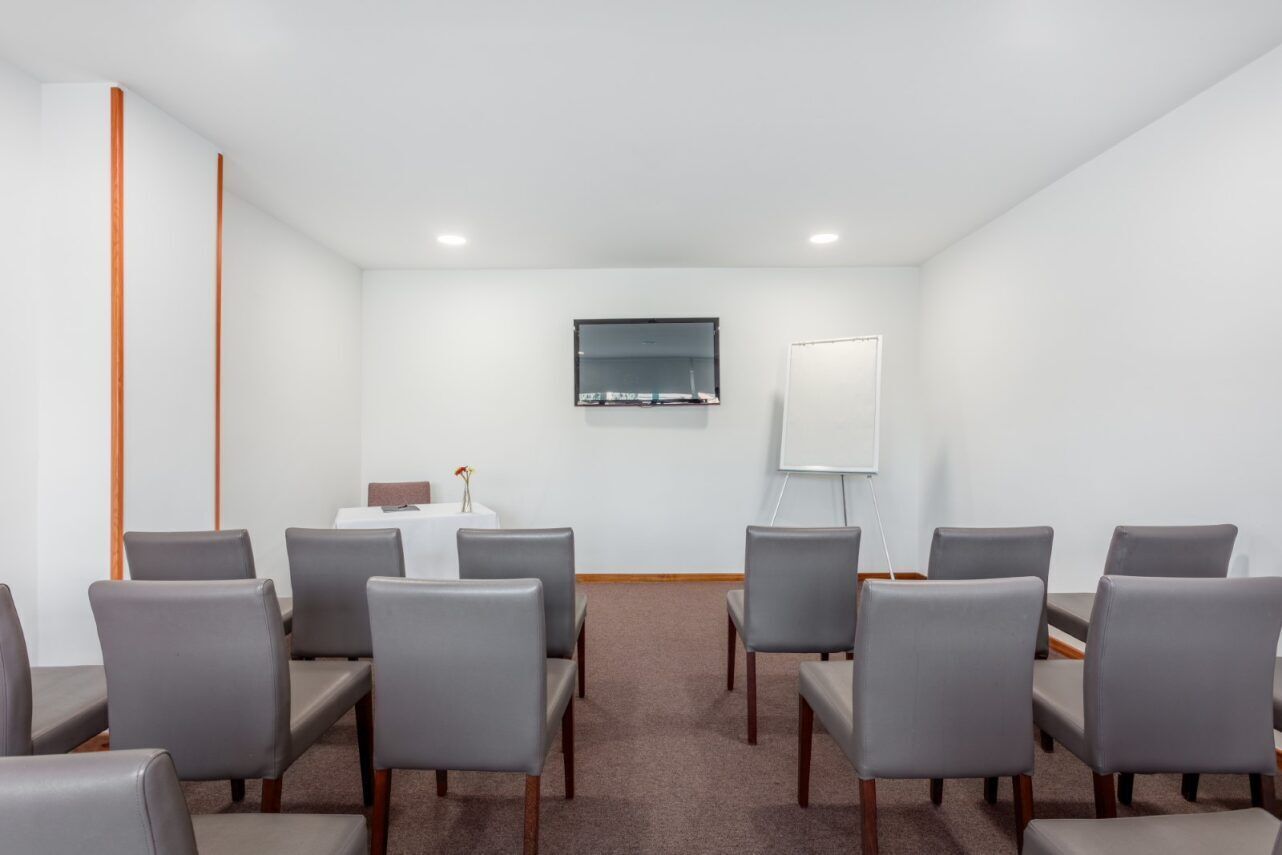 Ein Konferenzraum mit grauen Stühlen, einer Whiteboard-Tafel und einem Flachbildfernseher an der Wand.