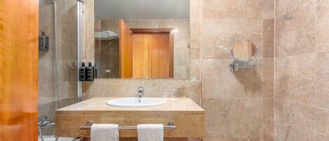 Un baño con lavamanos de mármol, cabina de ducha de vidrio y puerta de madera.