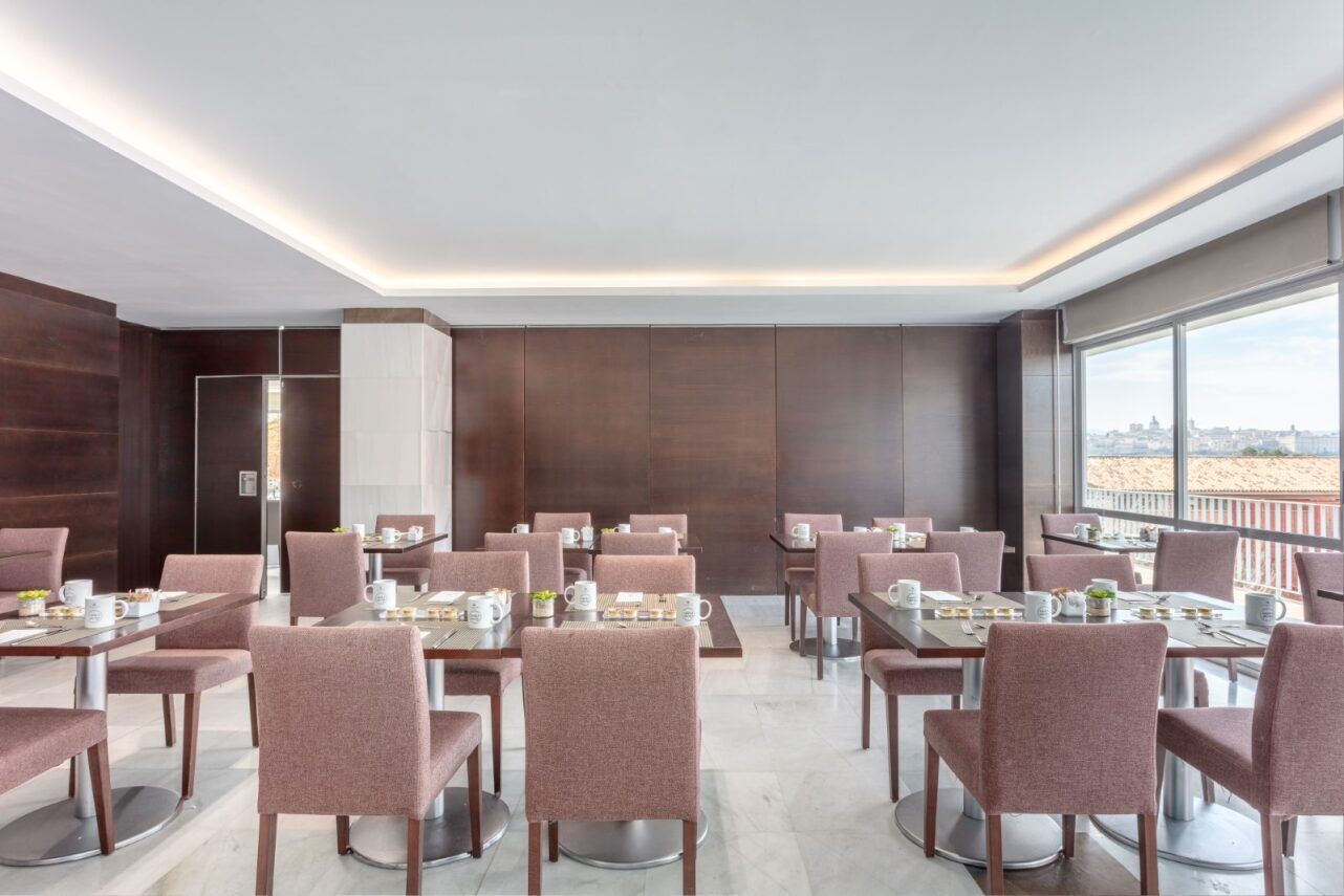 A modern dining area with multiple tables and chairs, large windows offering a view of the cityscape.