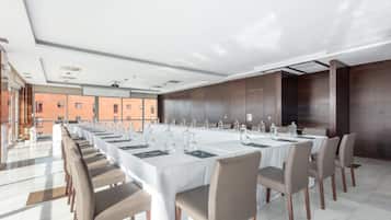 Un salón de conferencias con mesas largas y sillas, ventanas amplias y vistas a edificios.