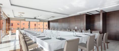 Un salón de conferencias con mesas largas y sillas, ventanas amplias y vistas a edificios.