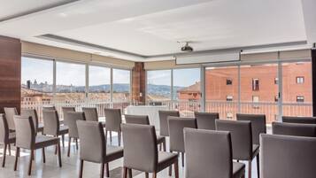 Un salón de conferencias con vista a la ciudad, grandes ventanales y un ventilador de techo.