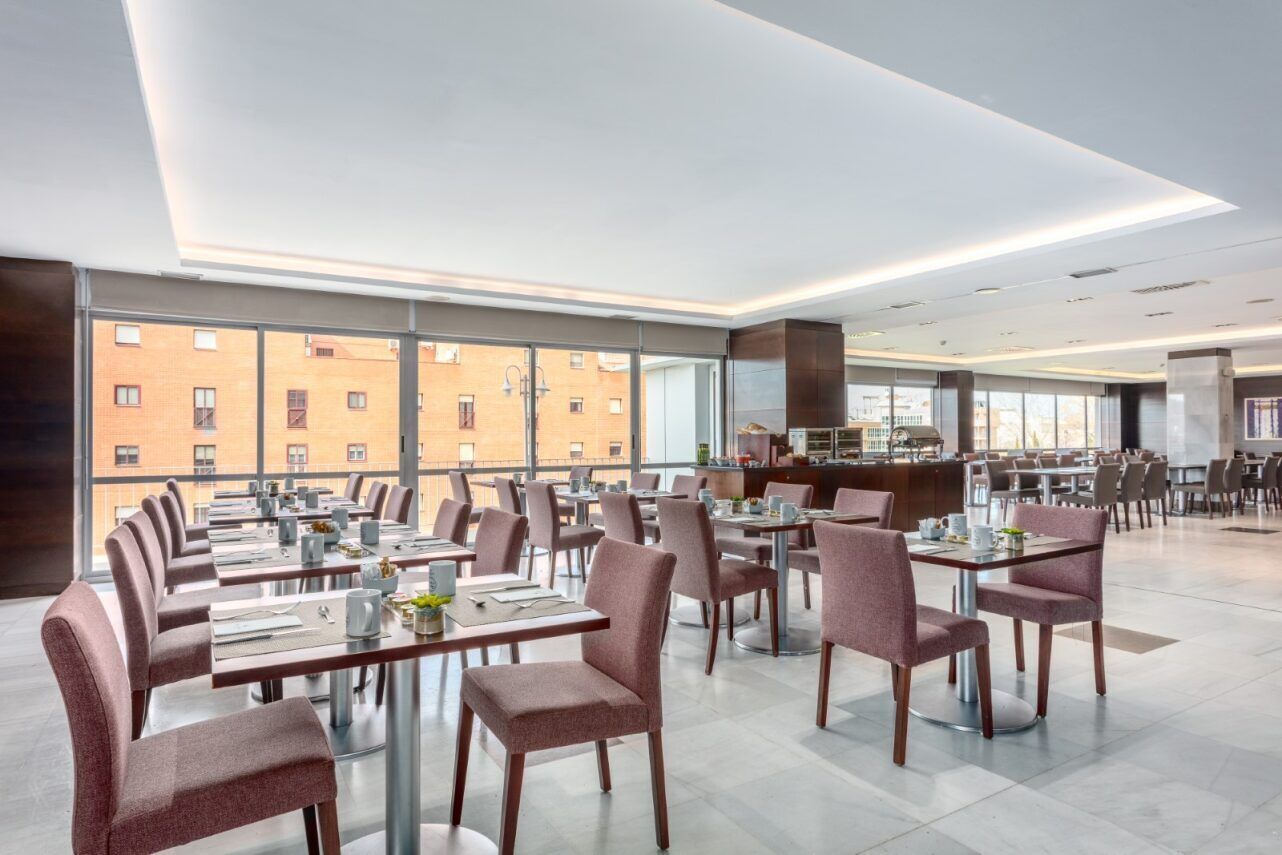 Un comedor moderno con mesas y sillas, ventanas amplias y vistas a edificios.