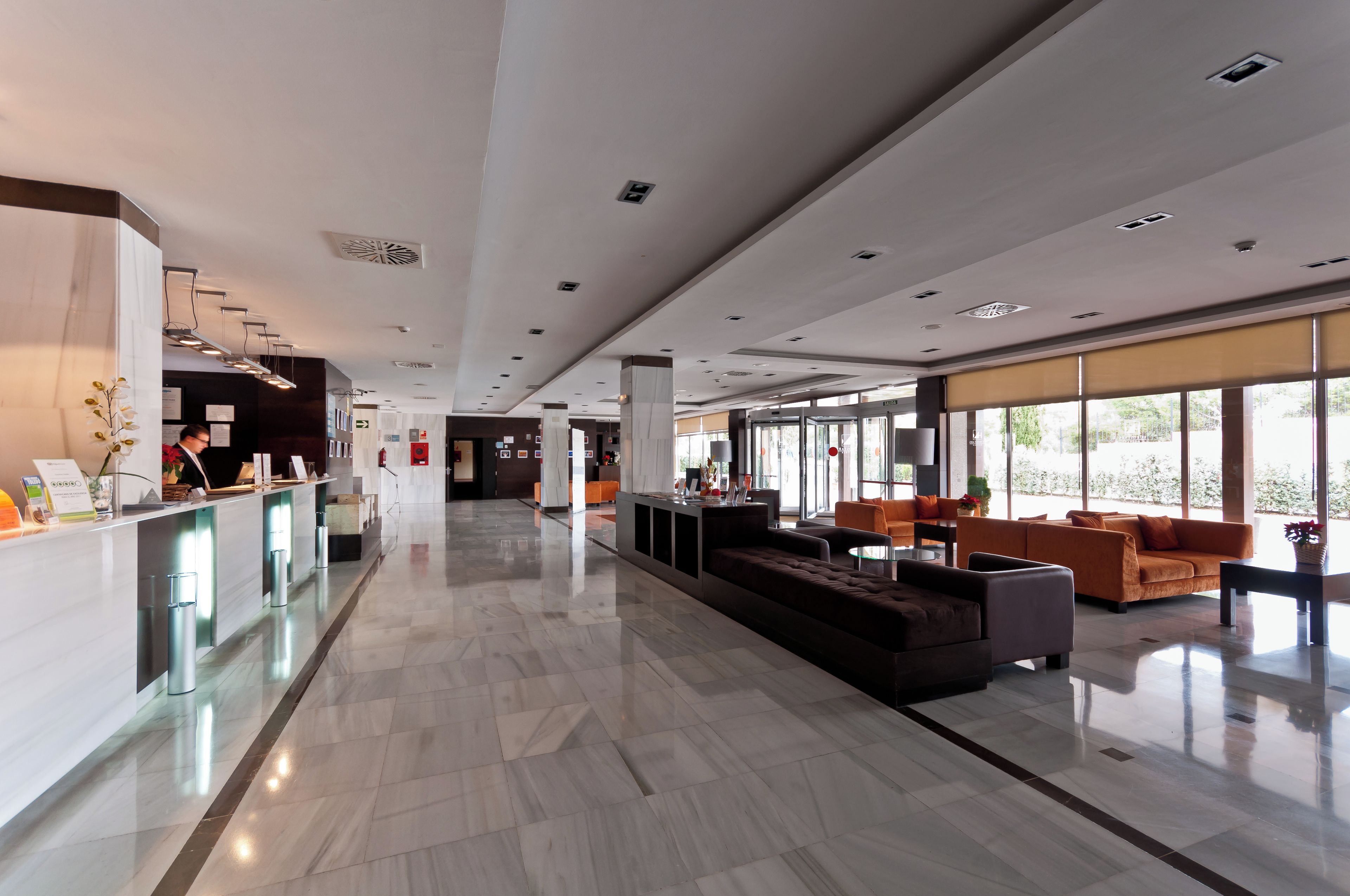 Un hall amplio con mostrador de recepción, zona de estar y grandes ventanales.