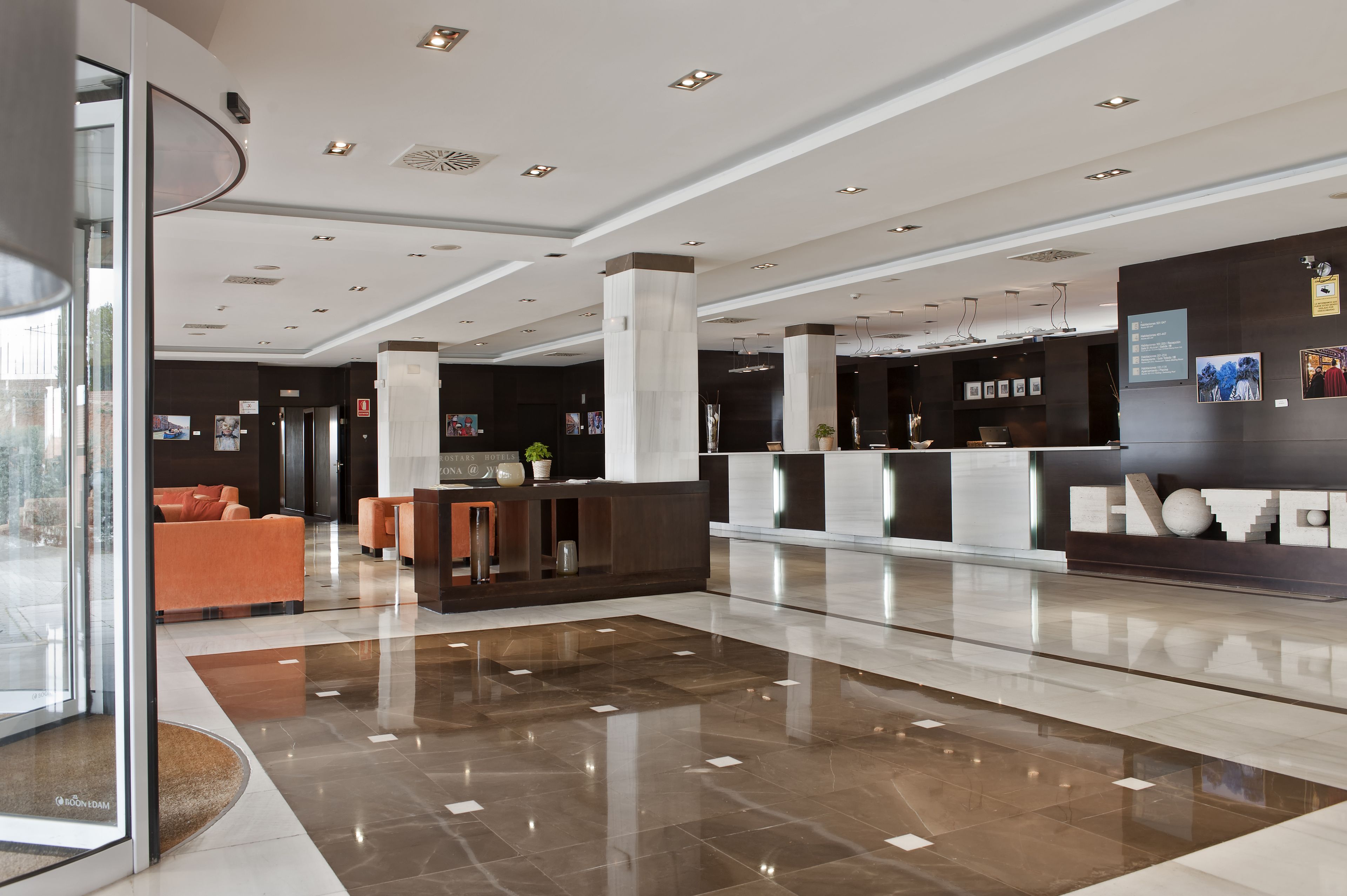 Un hall d’hôtel moderne comprenant un comptoir d’accueil, un espace salon et une entrée en verre.