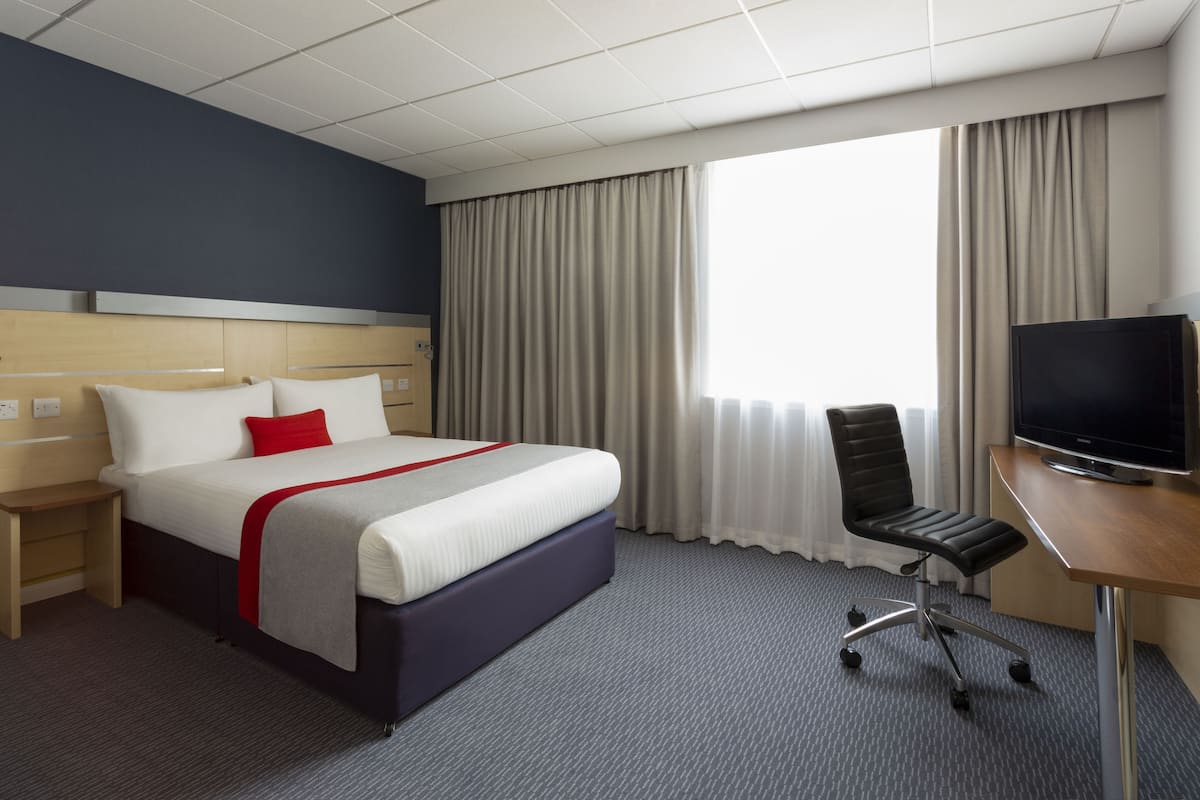 Ein Hotelzimmer mit Bett, Schreibtisch mit Fernseher, Stuhl und einem Fenster mit Vorhängen.