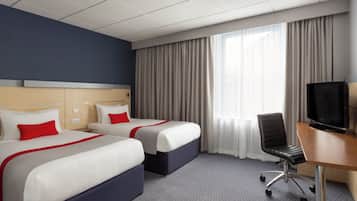 Habitación de hotel con dos camas, un escritorio con silla, televisor y un amplio ventanal con cortinas.