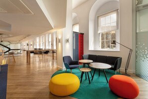 A modern interior with a long corridor, seating area with round tables, and large windows. - Holiday Inn Express - Edinburgh City Centre by IHG (Edinburgh)