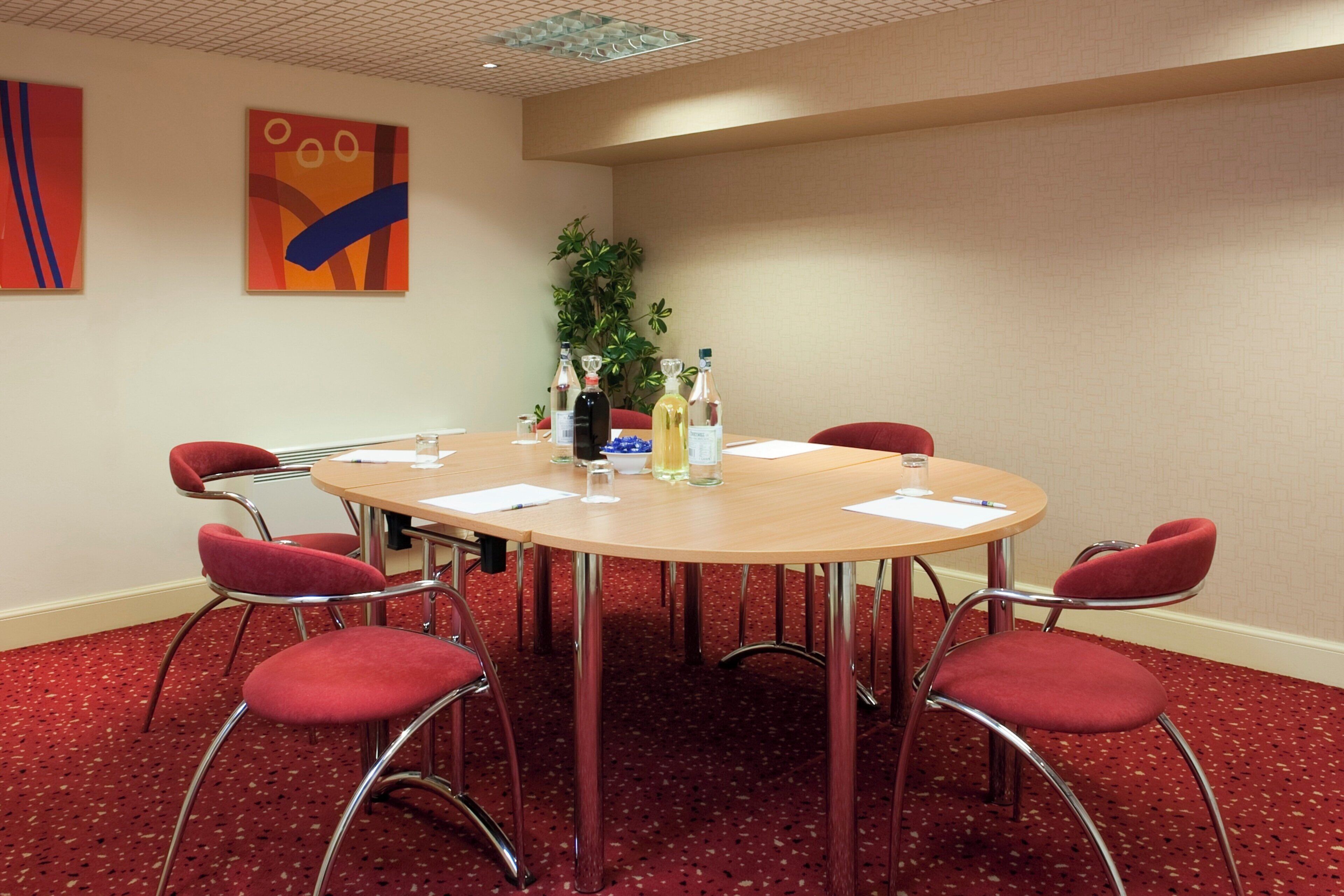 A conference room with a round table, six red chairs, and a potted plant.