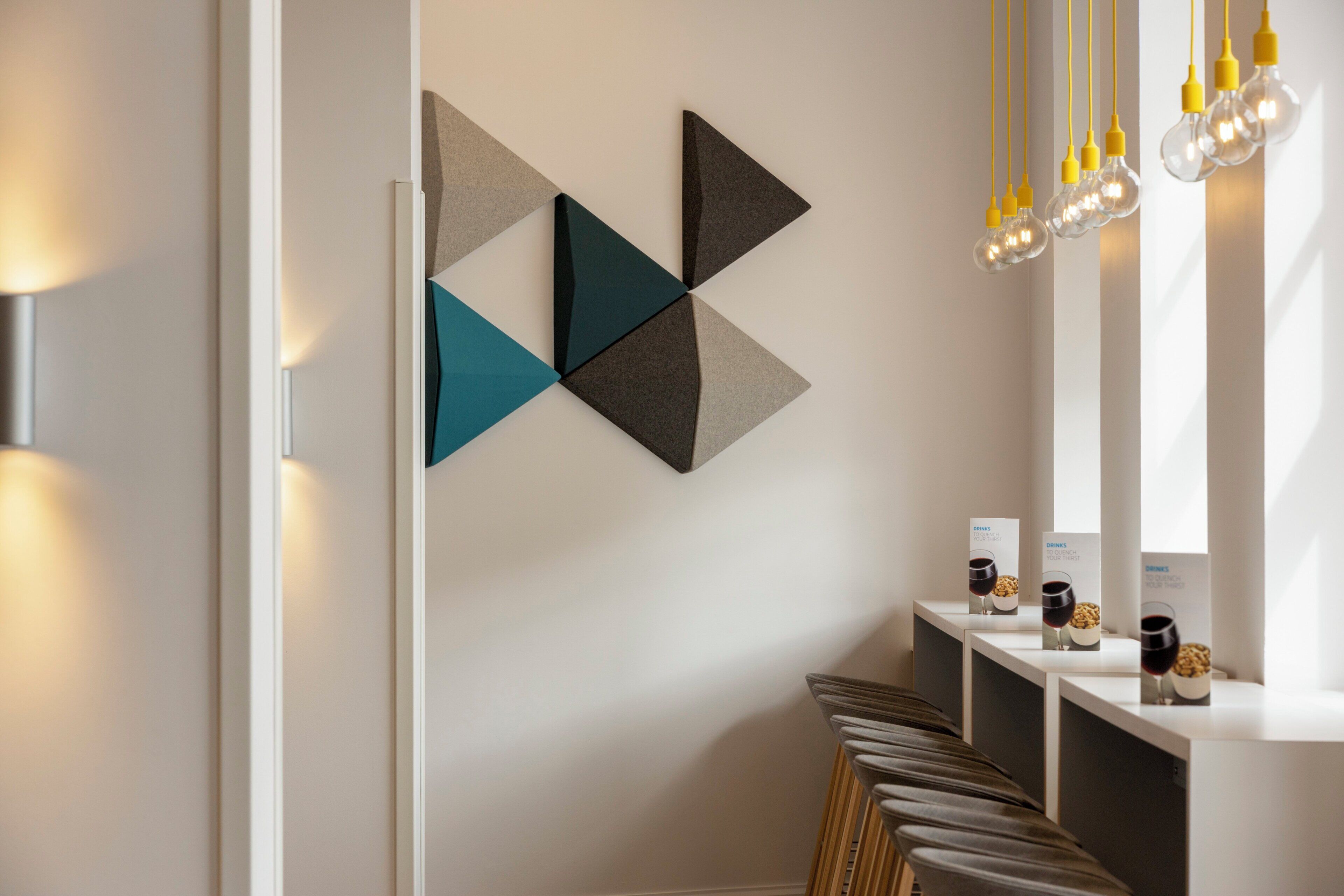 A modern interior with geometric wall art, a row of bar stools, and a bar area with a wine glass and bottle.