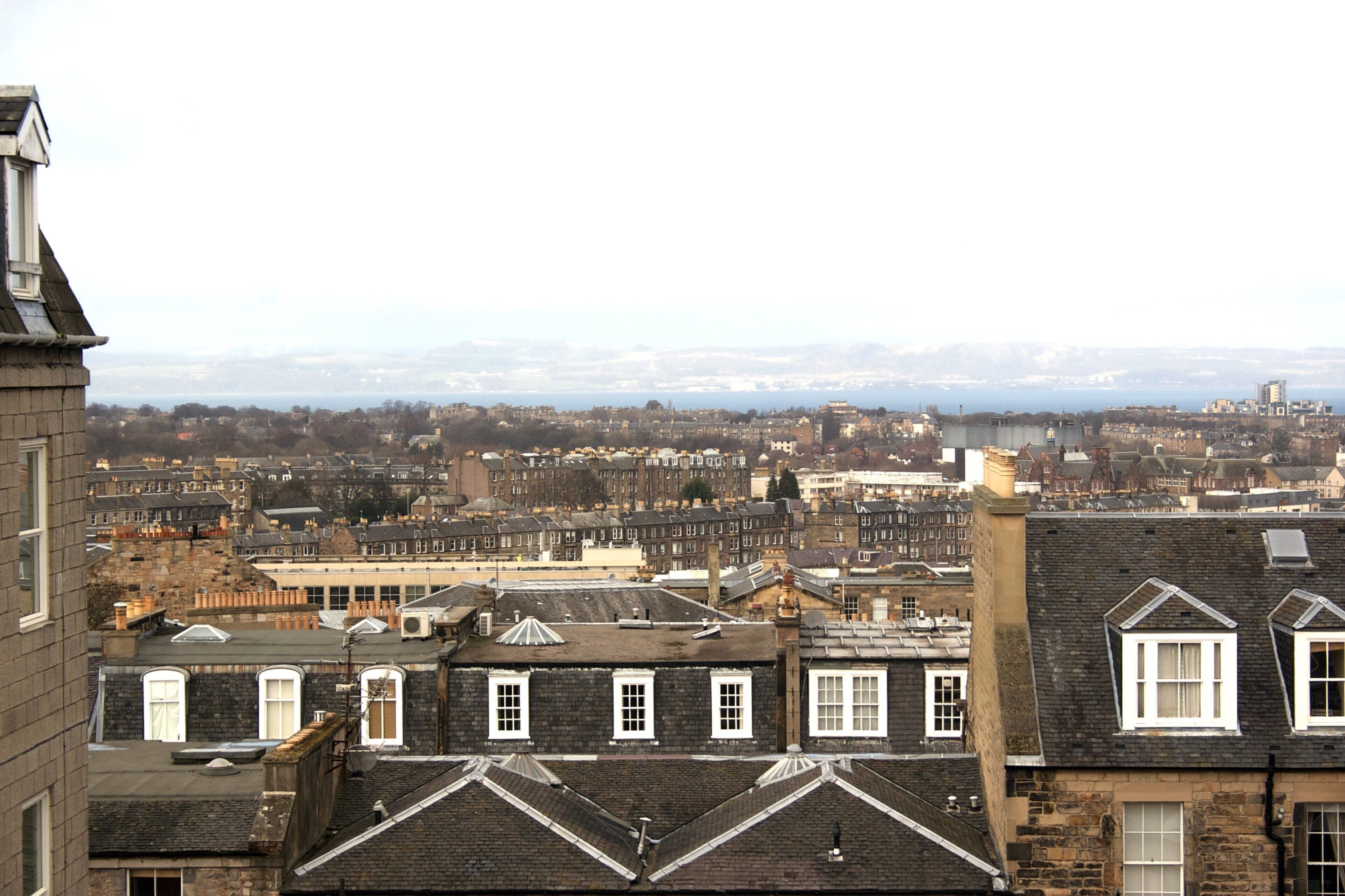 A cityscape with a mix of residential and commercial buildings, including a prominent stone building with a pitched roof and dormer windows.