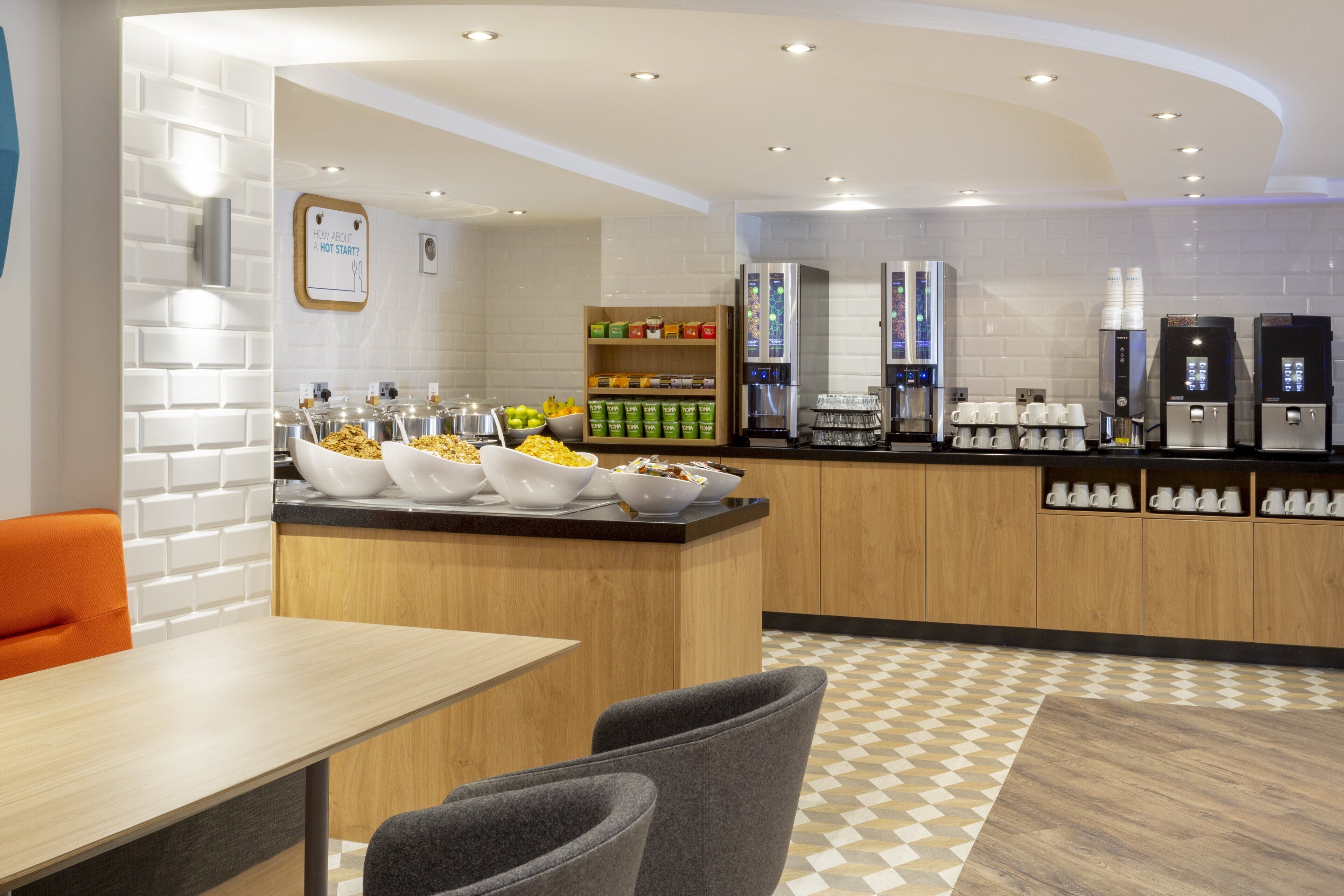 A modern breakfast bar with a variety of food options, a coffee station, and a seating area with a checkered floor pattern.