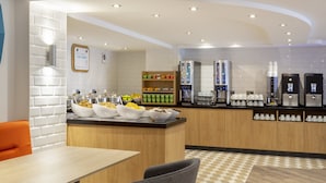 A modern breakfast bar with a variety of food options, a coffee station, and a seating area with a checkered floor pattern.