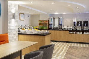 A modern breakfast bar with a variety of food options, a coffee station, and a seating area with a checkered floor pattern.