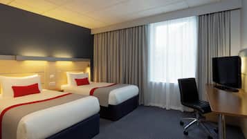 Habitación de hotel con dos camas, un escritorio con silla, televisor y un ventanal con cortinas.