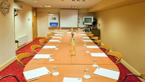 A conference room with a long table, chairs, a clock, a welcome sign, and a television.