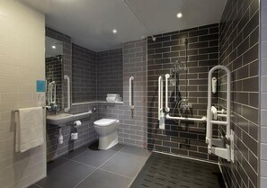A modern bathroom with a toilet, sink, and shower area, featuring dark tiles and handrails. - Holiday Inn Express - Edinburgh City Centre by IHG (Edinburgh)