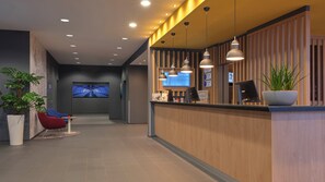 Zona de recepció d'hotel amb un taulell de recepció de fusta, una pantalla digital que mostra el nom de l'hotel i una zona de seients amb cadires.