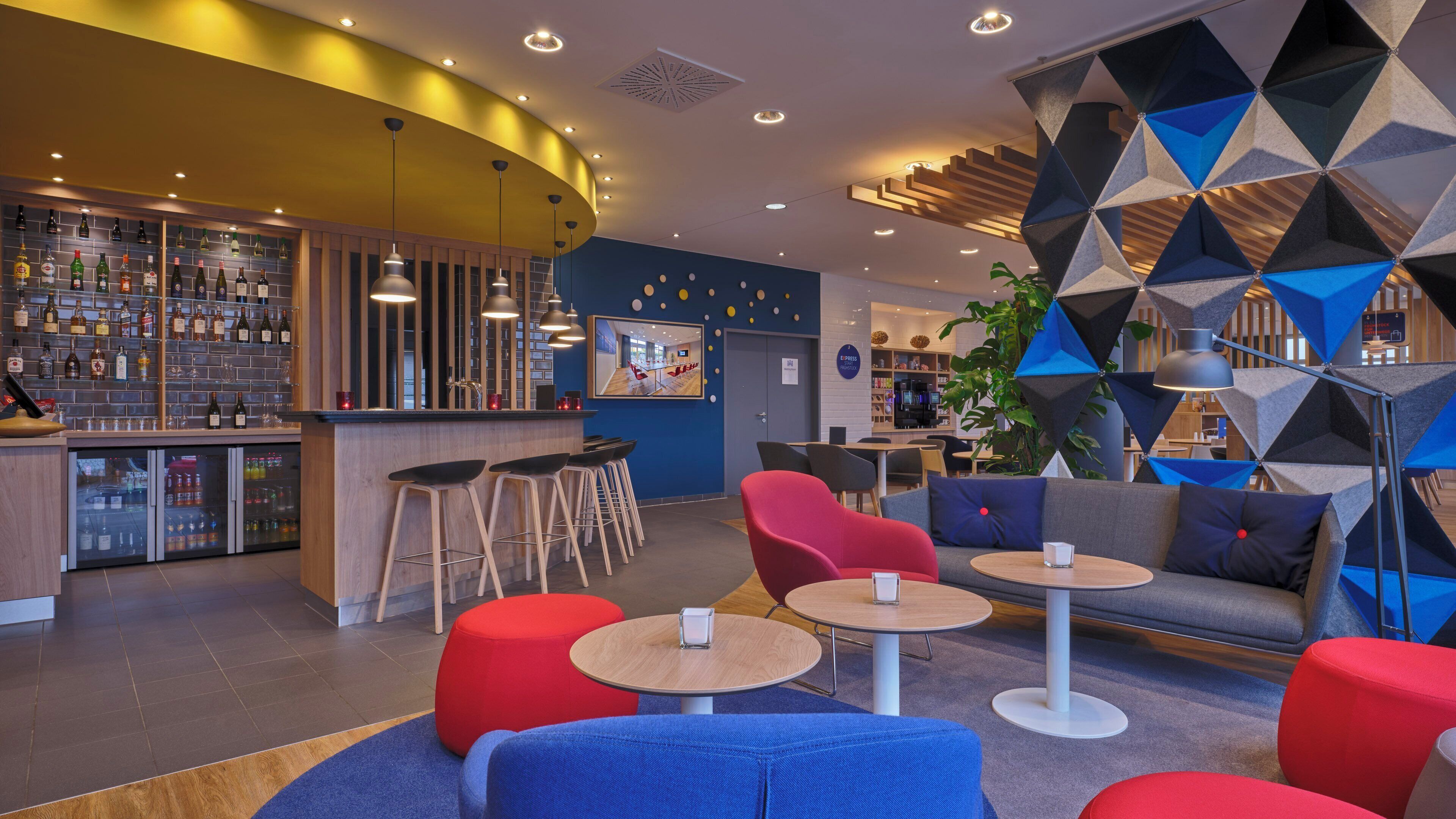 A bar area with stools, a seating area with round tables and sofas, and a decorative wall with geometric patterns.