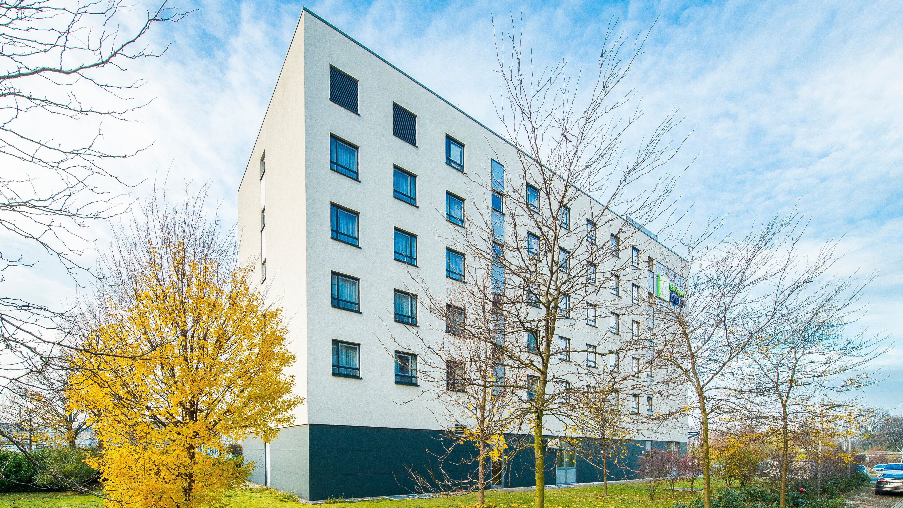 Een modern meerlaags gebouw met een platte gevel, veel ramen en een groene basis.