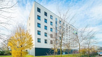 A modern multi-story building with a flat facade, numerous windows, and a green base.