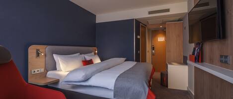A hotel room with a bed, a TV, a desk, and a chair.