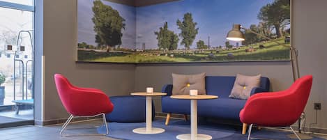 A room with a blue sofa, two red chairs, a small table, and a large landscape painting on the wall.