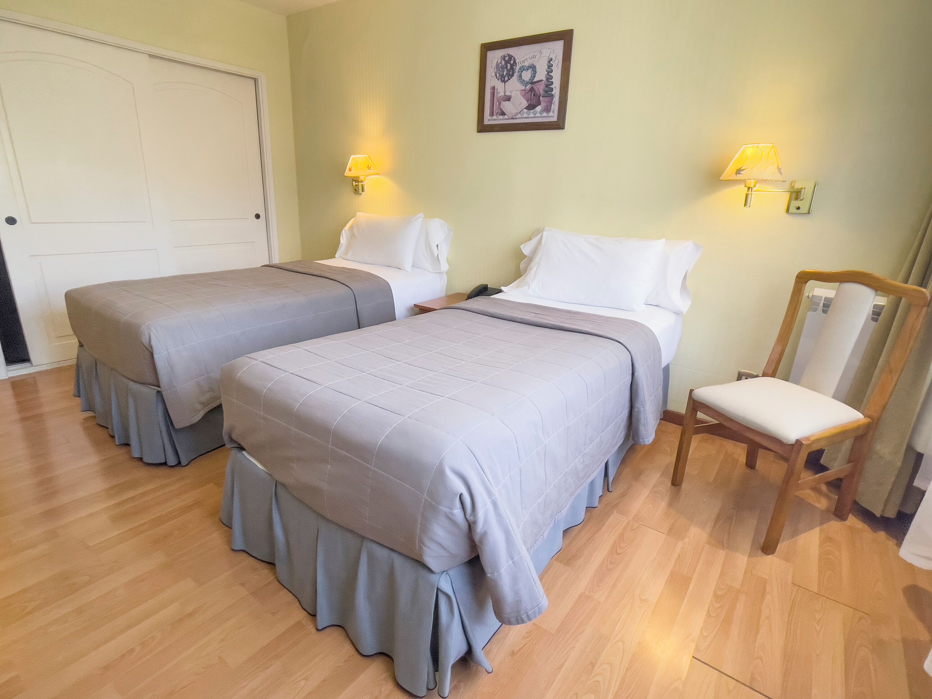 A hotel room with two beds, a wooden chair, and a door.