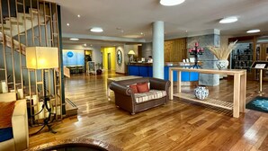 Un hall d’entrée spacieux avec un plancher en bois, un comptoir de réception, un canapé, une table basse et un élément décoratif aquatique.