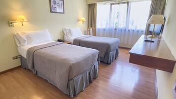 Habitación de hotel con dos camas, un escritorio y una ventana con cortinas.