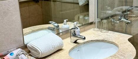 A bathroom with a curved granite sink, a mirror, and a glass shower enclosure.