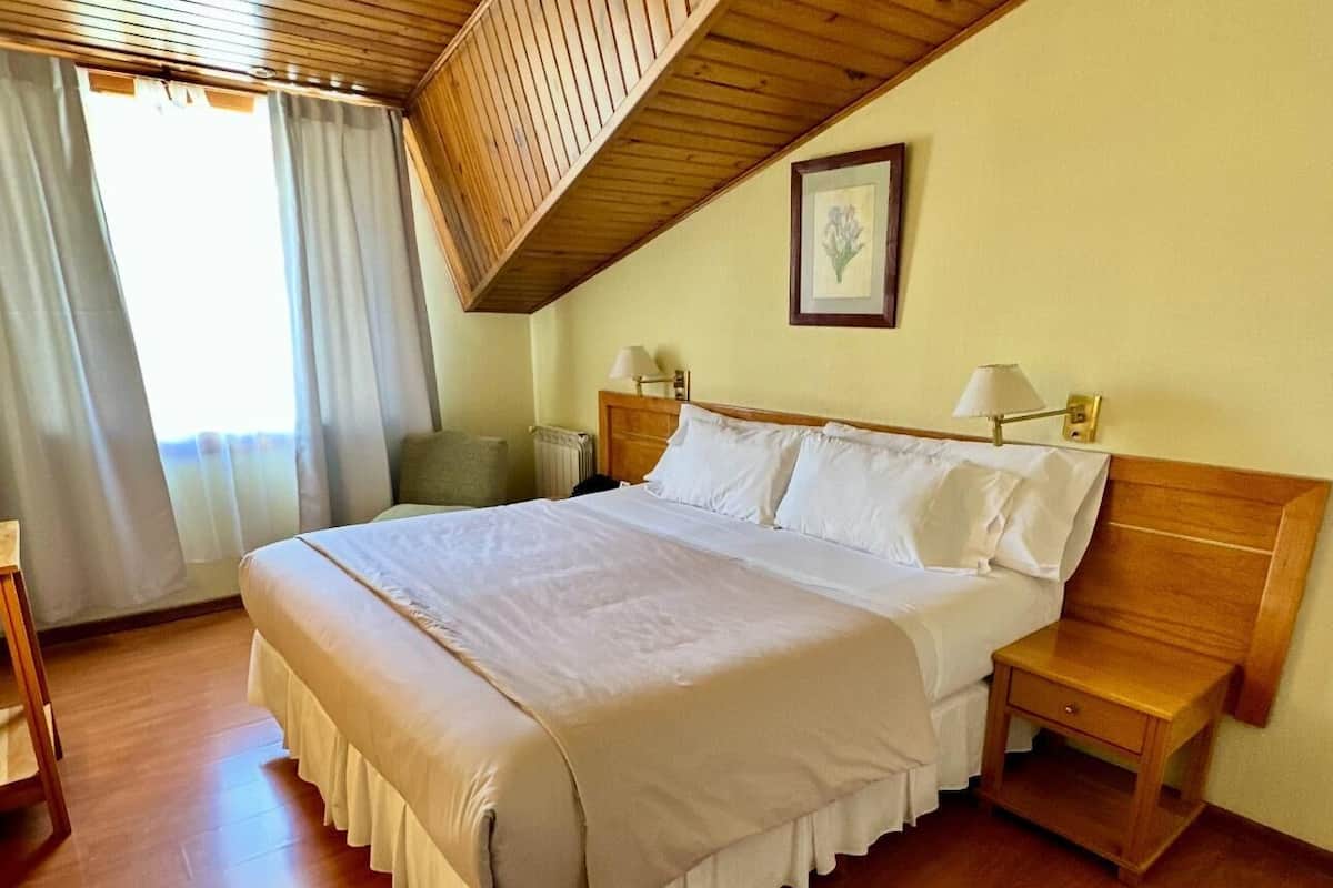Una cama bien hecha en una habitación con suelo de madera y techo inclinado.