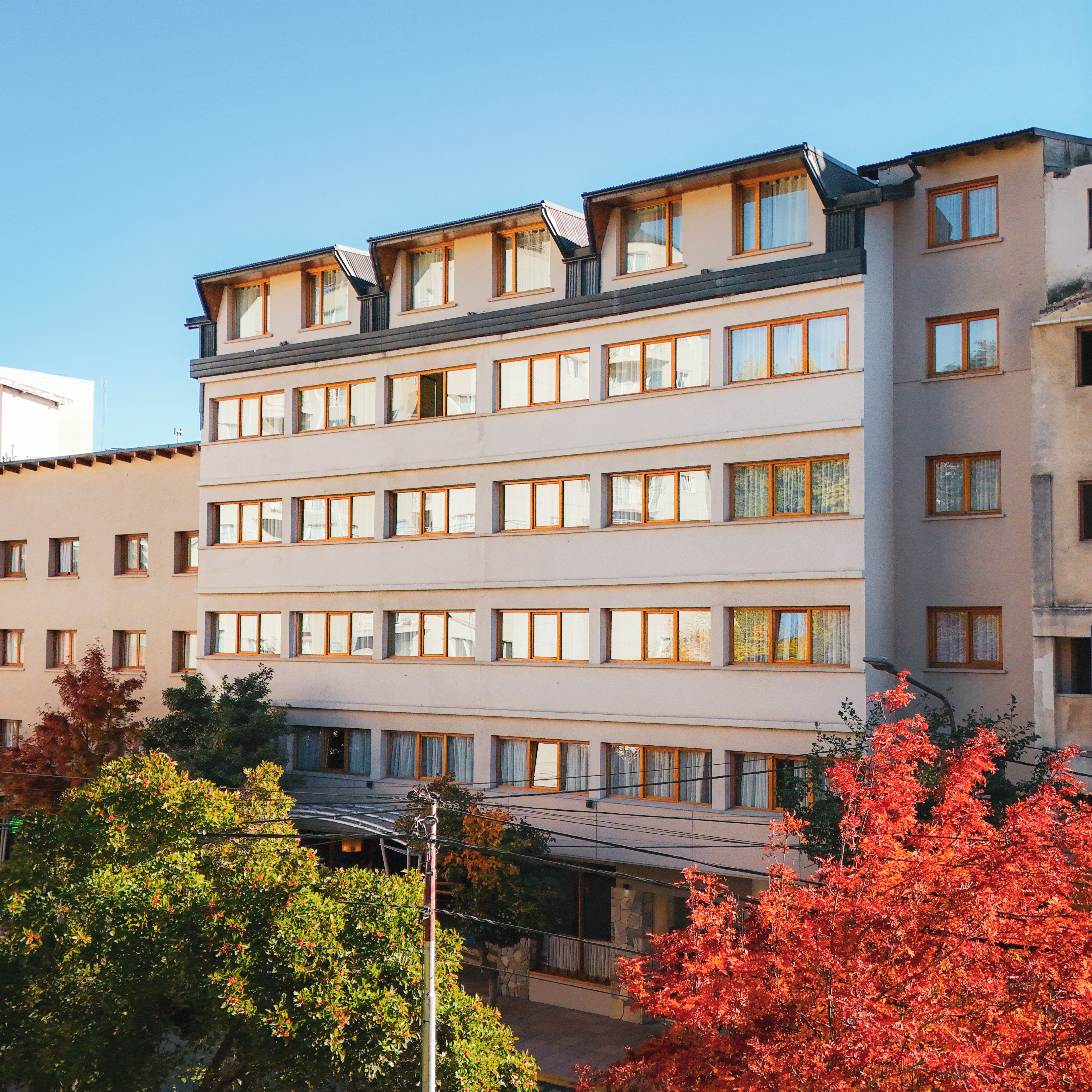 A multi-story hotel with a flat facade, numerous windows, and a parking area in front.