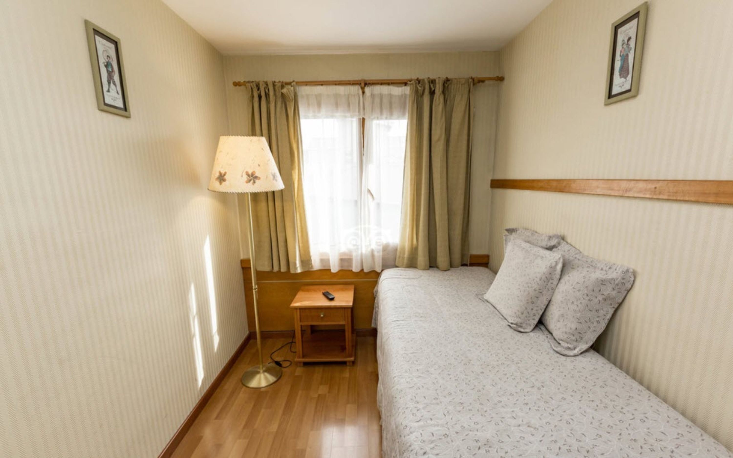 Un dormitorio pequeño y ordenado con una cama individual, una mesita de noche, una lámpara y una ventana con cortinas.