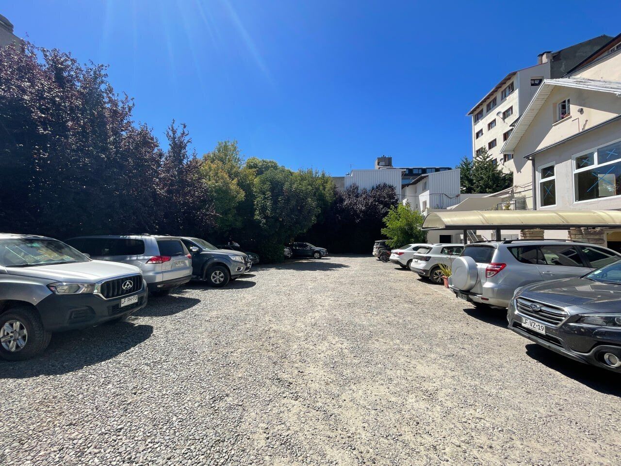 Un estacionamiento con varias camionetas SUV y automóviles, rodeado de edificios y árboles.