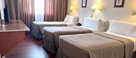 A hotel room with three beds, a desk, and a small ottoman.
