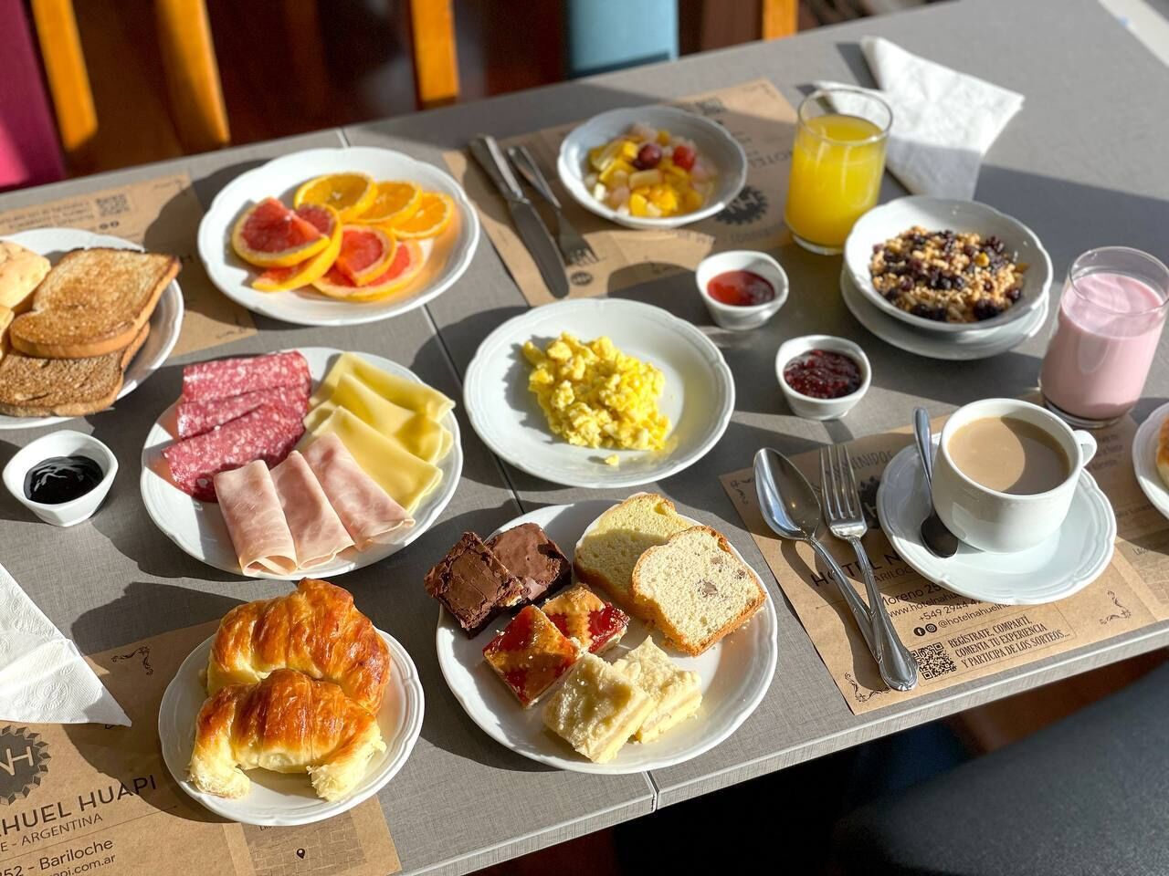 A breakfast table with various food items and drinks, including toast, scrambled eggs, sausages, and a croissant.