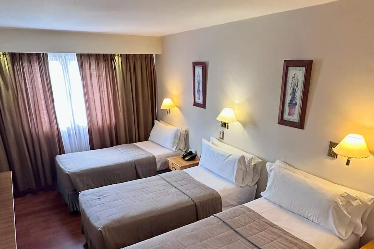 Habitación de hotel con tres camas individuales, suelo de madera, un escritorio y una silla.