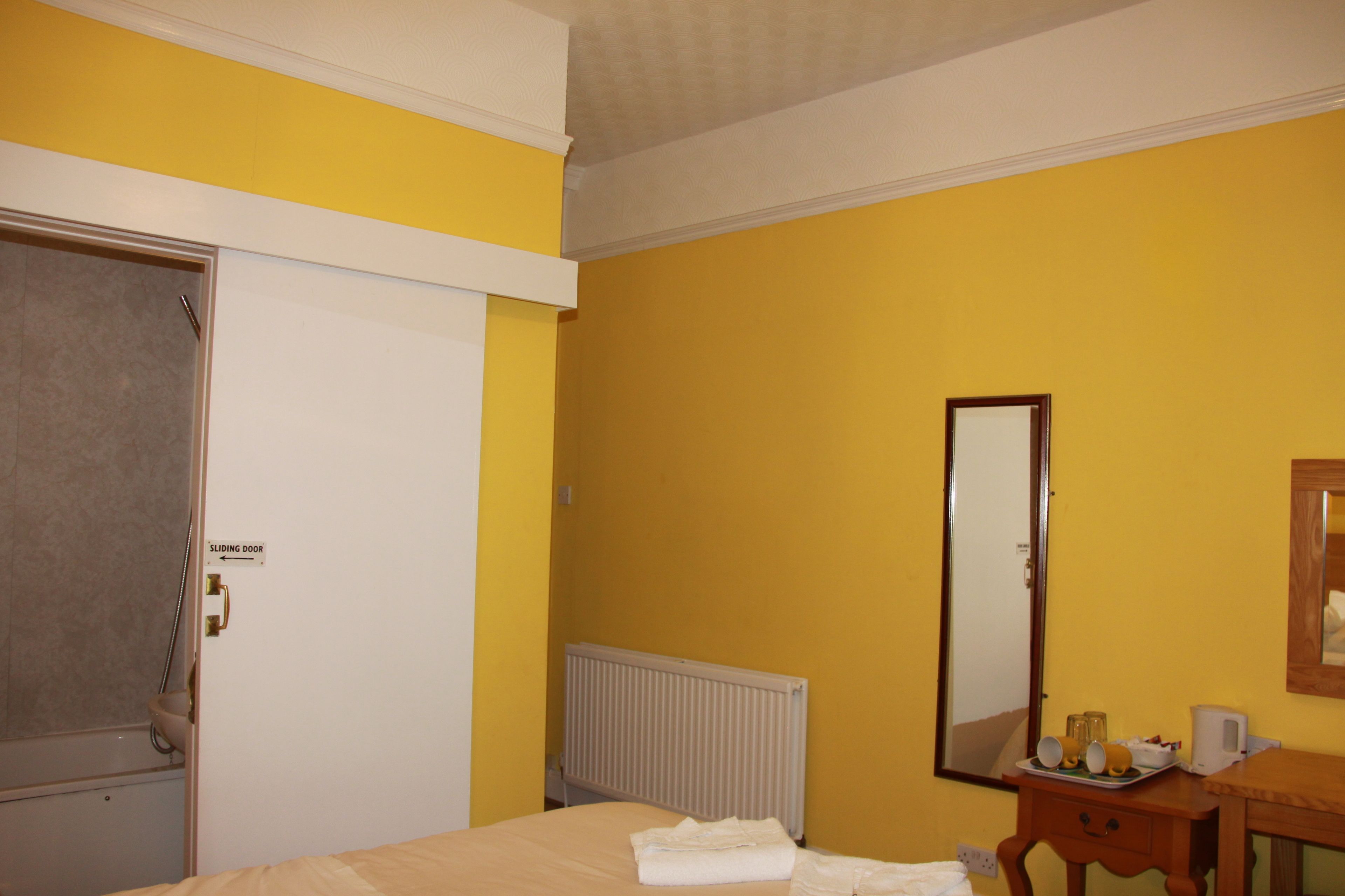 A hotel room with a bed, a bedside table with a tray of toiletries, a radiator, and a sliding door.