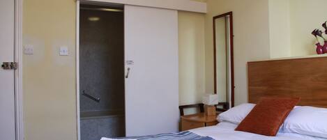 A hotel room with a bed, a wooden headboard, a nightstand, a mirror, and a sliding door to a bathroom.