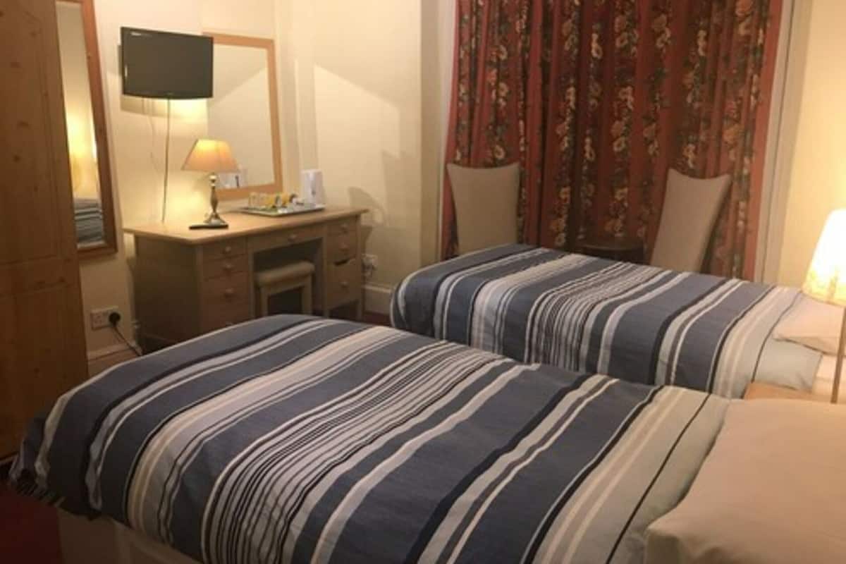 Habitación de hotel con dos camas, un escritorio, una silla, un televisor y una ventana con cortinas.