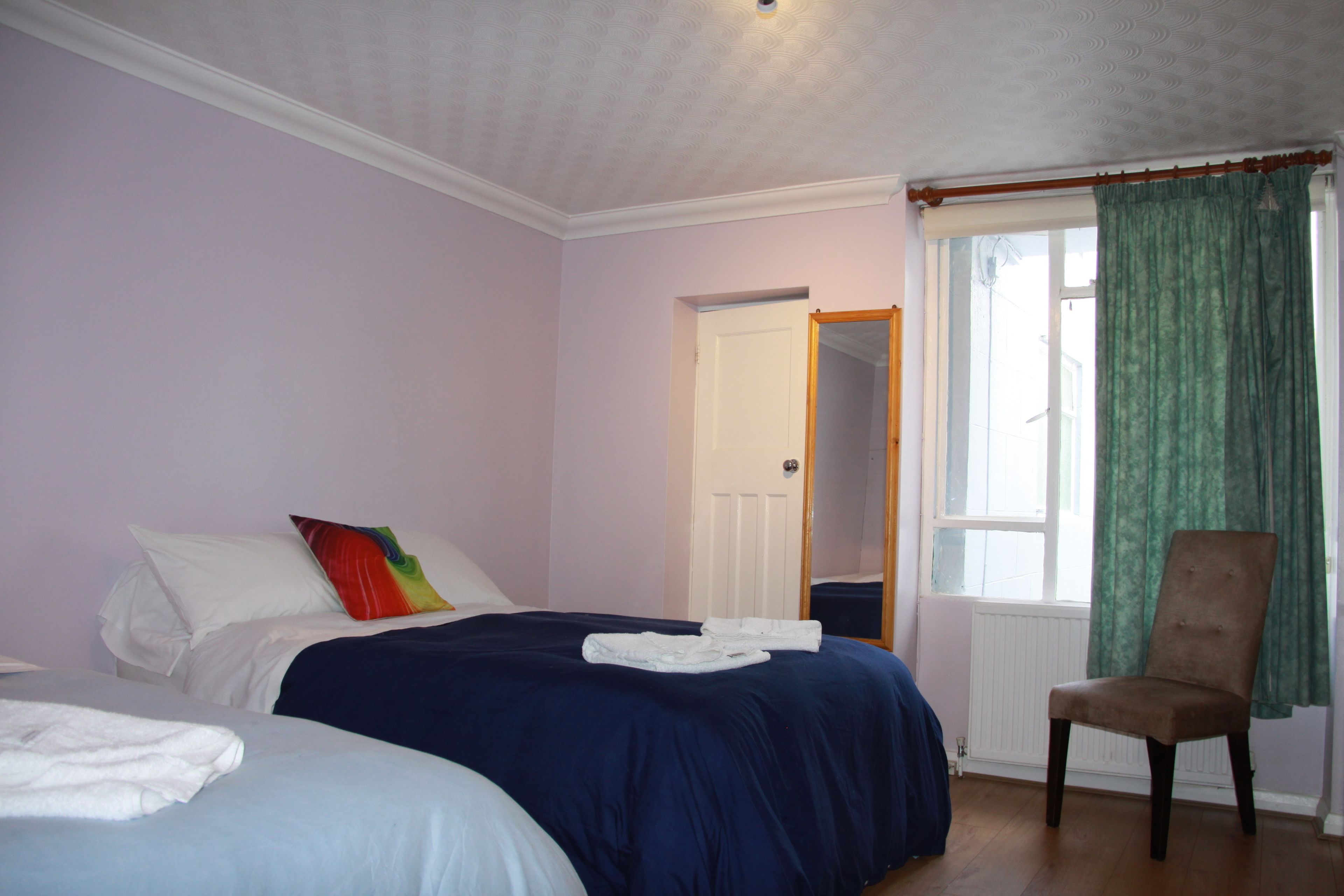 A bedroom with two beds, a chair, and a window with curtains.