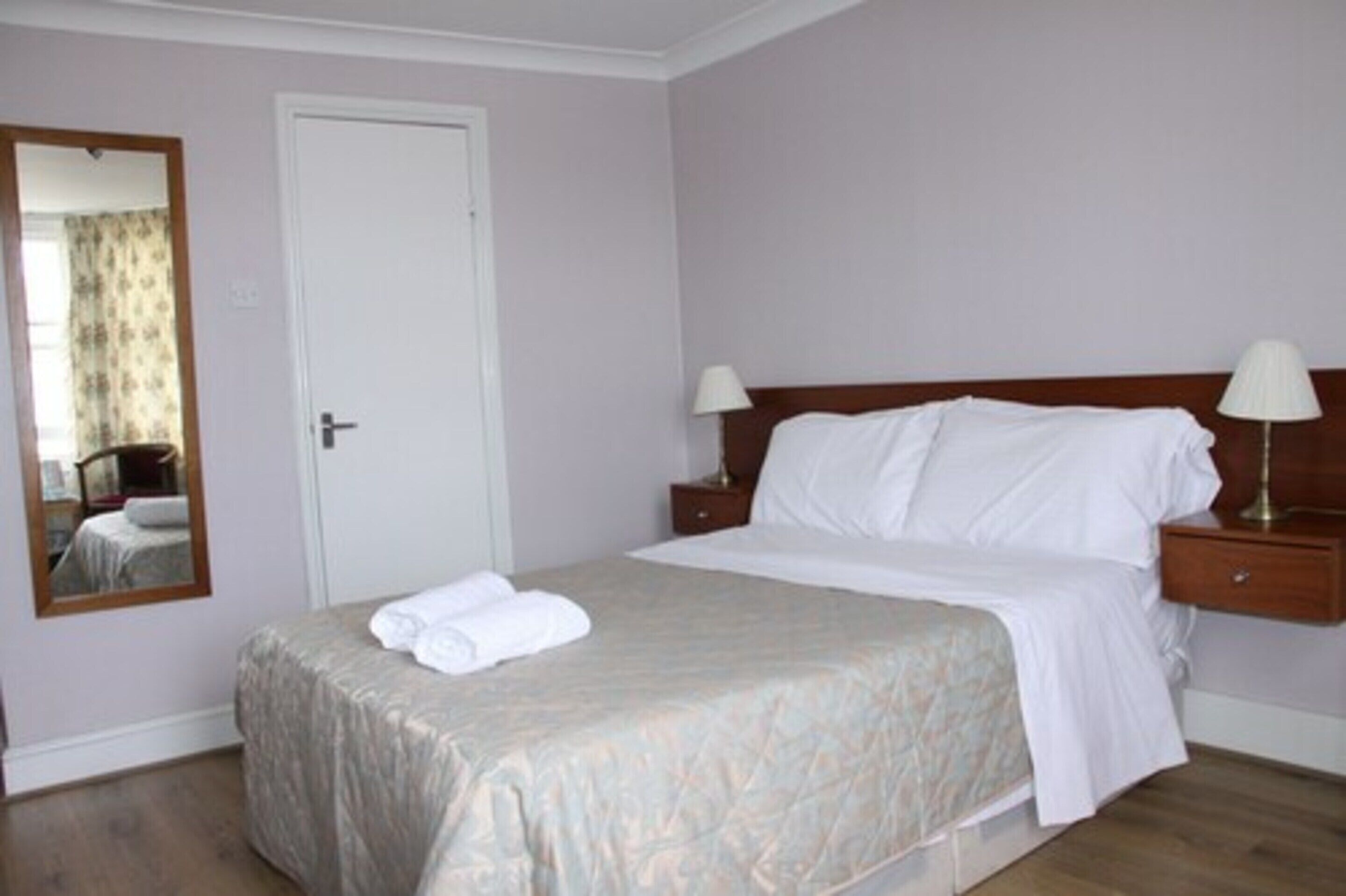 A neatly made bed with white linens, a bedside table with a lamp, and a mirror on the wall.