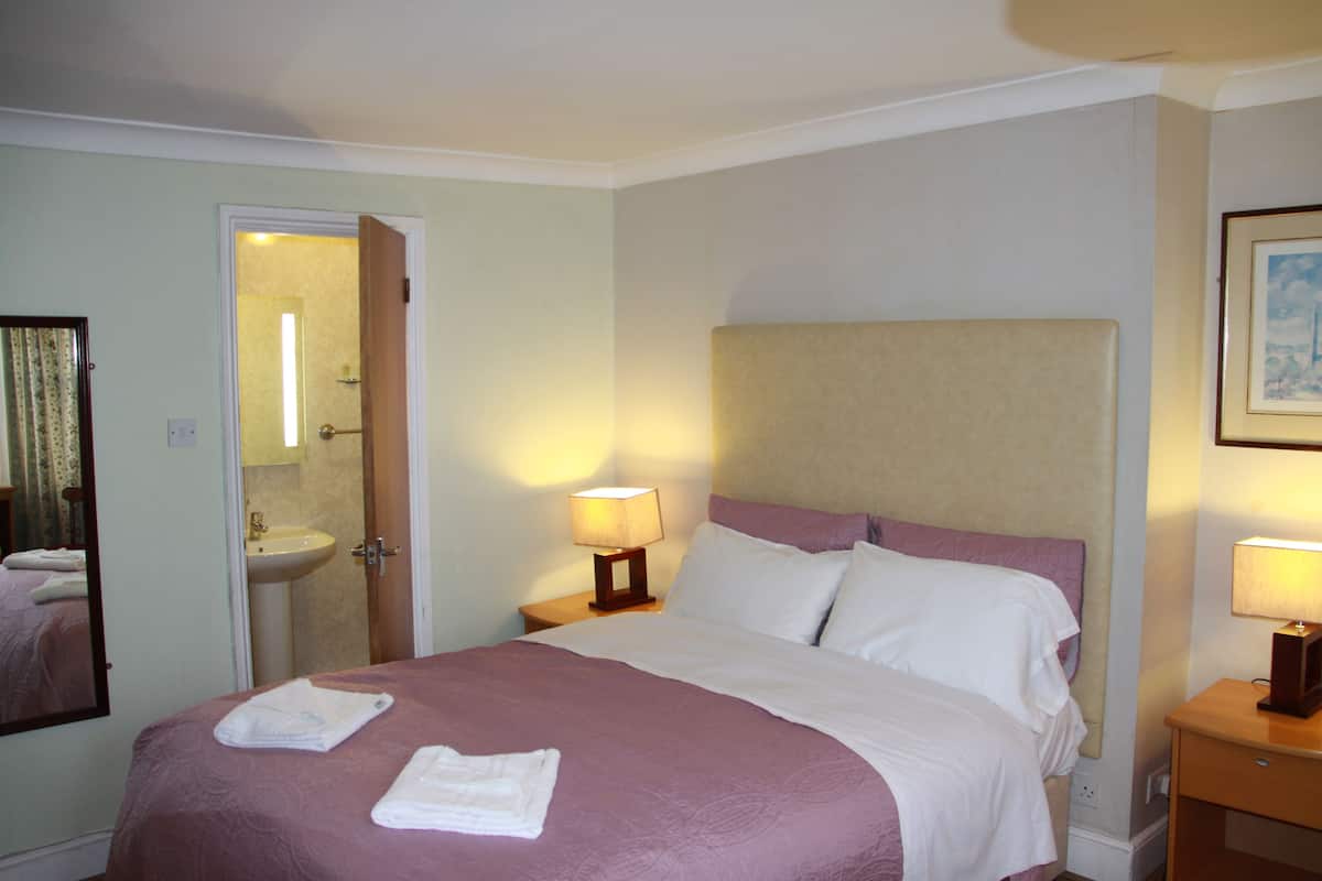Una habitación de hotel con una cama, una mesita de noche, una lámpara de noche, un espejo y una puerta que da a un baño.