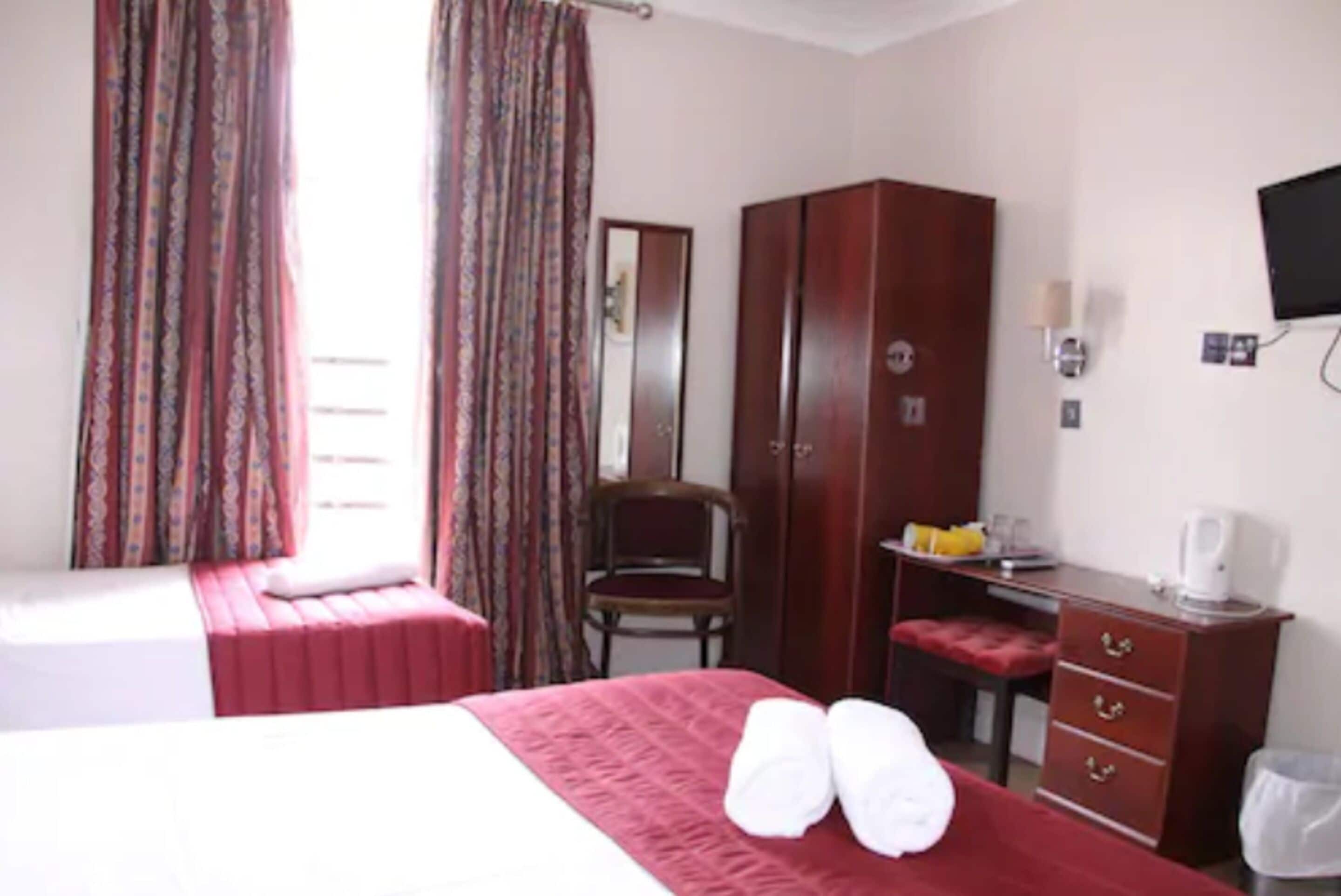 Una habitación de hotel con cama, armario, escritorio con silla y televisor en la pared.