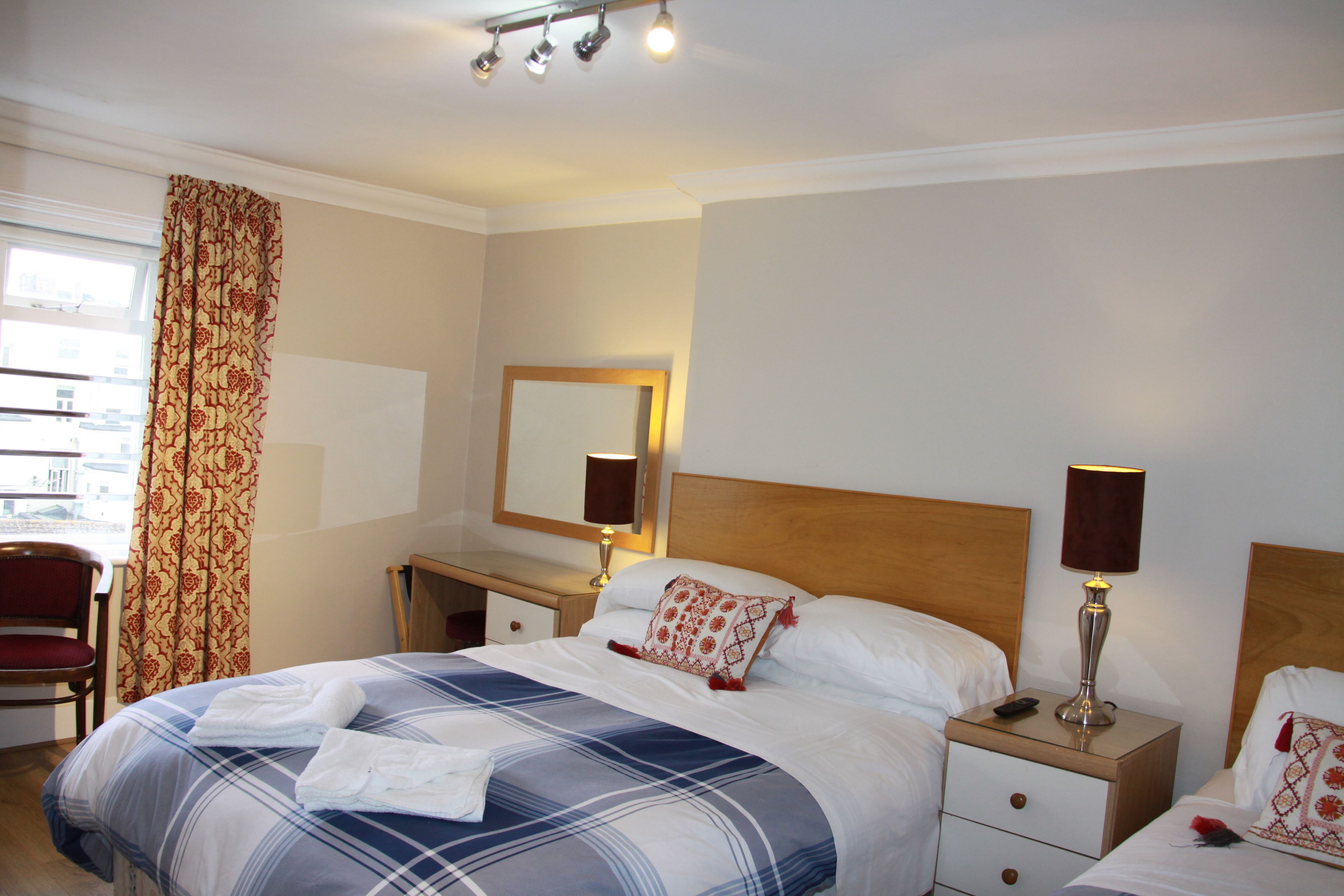 A hotel room with a bed, two bedside tables, a chair, a window with curtains, and a mirror on the wall.