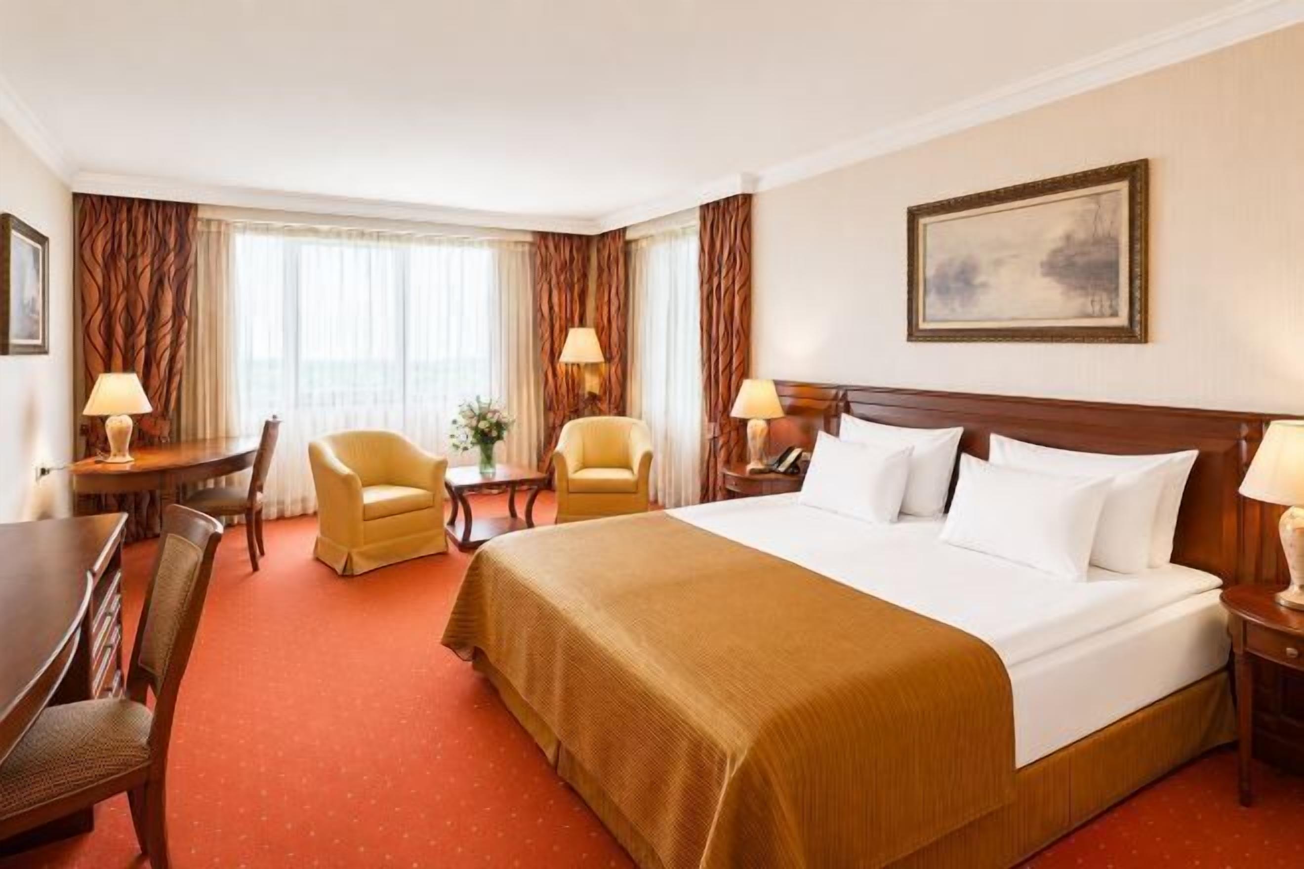 A hotel room with a large bed, two armchairs, a desk, and a nightstand.